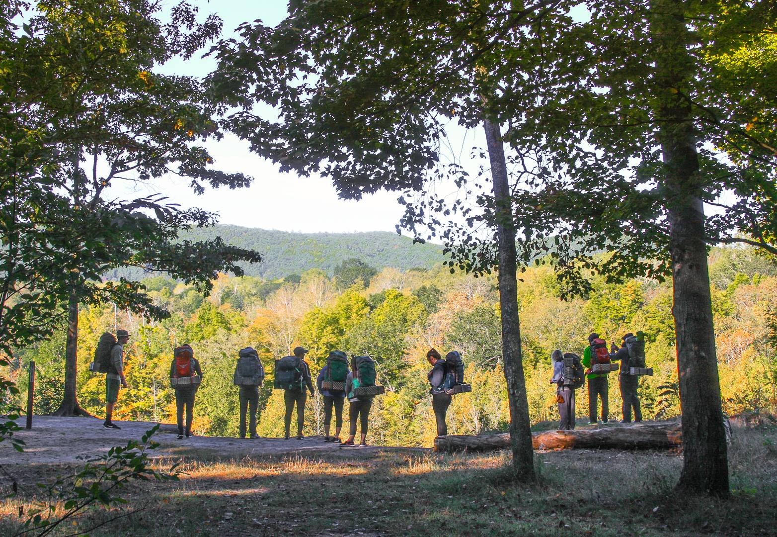 10 students with backpacks standing at the edge of a cliff overlooking the Manistee river